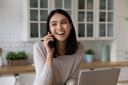 Happy beautiful young korean asian woman listening good news involved in pleasant phone call conversation, distracted from computer work, talking speaking with friends, distant communication concept.