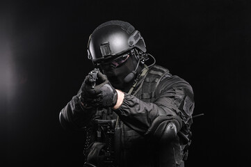 A man in glasses, a helmet and a bulletproof vest aims at the camera, photo on a black background.