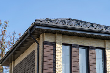 Tiled roof with segment of snow holding structure, Gutter system for metal roof. House with new grey metal tile roof and rain gutter. Metallic Guttering System, Guttering and Drainage Pipe Exterior