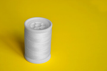 Reel of white sewing threads on yellow background. Copy space, close-up.