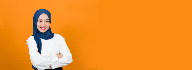 Banner of smiling Asian young Muslim woman in hijab head scarf standing against orange colour background
