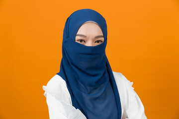 Portrait of Asian muslim woman wearing the face veil on orange colour background in studio
