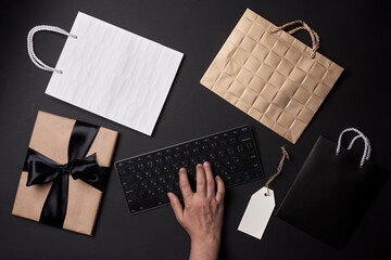 Black Friday concept. Shopping online. A person ordering gifts, clothes and other items in online shop. Shopping bag, gift box, computer keyboard from above