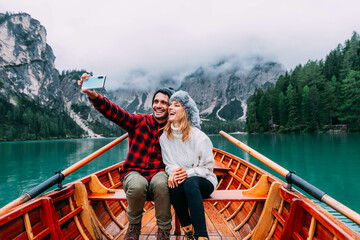 Romantic couple of adults in love taking selfie on a boat visiting an alpine lake at Braies, Italy...
