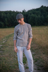Portrait of an 18-year-old boy in a cap, standing on a dirt road .