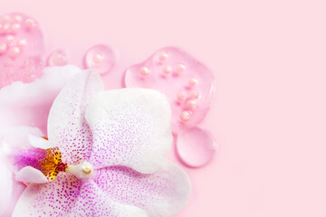 Fototapeta na wymiar Orchid flower with transparent serum blobs and particals on pink background. Beauty product macro concept