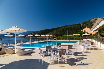 Fototapeta na wymiar Luxury swimming pool with empty deck chairs, tables and umbrellas at the resort with beautiful sea view. Greek island.