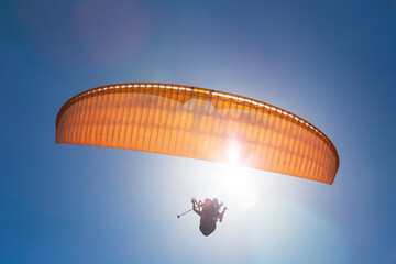 Tandem orange paragliding against a blue sky, sunny day.