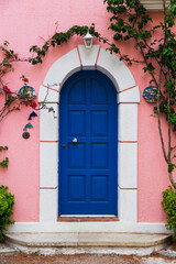 Fototapeta na wymiar Traditional greek house with colorful blue door and pink walls at Asos village. Assos peninsula famous and extremely popular travel destination in Cephalonia, Greece, Europe