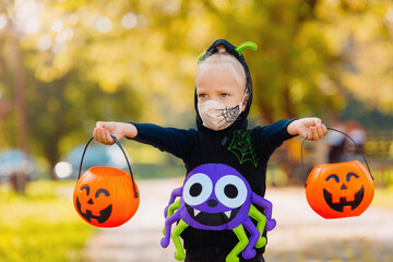 A child on the day of Happy Halloween weighs the collected sweets, wears a protective decorated mask