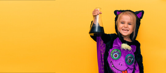 Halloween games for young children. A child in a bat costume looks at a flask with a black liquid on a yellow-orange background. banner with place for text