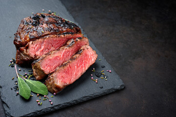 Barbecue dry aged wagyu rib-eye beef steaks with herb and black salt served as close-up on a black...