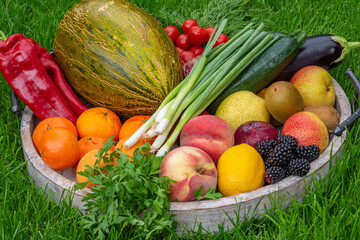 Fruits and vegetables in a wooden tray on green grass as background