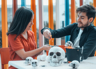 Jovenes adolescentes repartiendo caramelos en una cafeteria infantil con decorativas calaveras de juguete y dulces