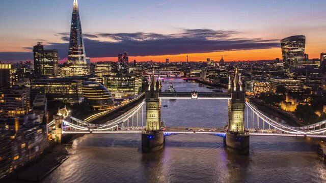 Forwards reveal of city lights of large town at dawn. Amazing hyperlapse of fly over Tower Bridge. Modern skyscrapers on both Thames river banks. London, UK