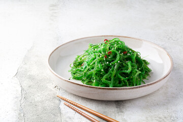 Green Chuka Seaweed, Wakame salad with sesame seeds in a plate with chopsticks on grey table....