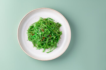 Green Chuka Seaweed, Wakame salad with sesame seeds in a plate on green pastel background. Healthy...