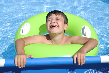 niño desdentado riendo en la piscina con un flotador verde