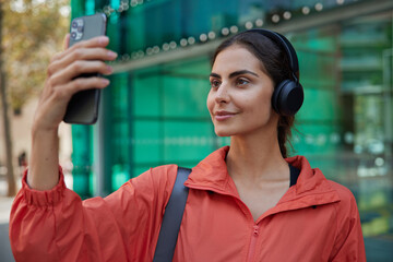 Athletic fitness trainer uses webcam to talk on video call has distant lesson records video for blog wears sportsclothes poses at city background. Satisfied European female watches yoga class online.