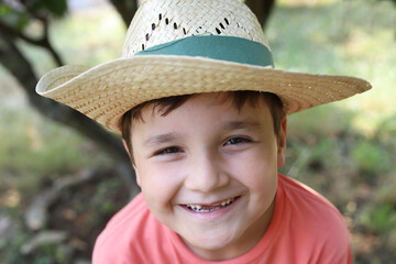 niño con gorro de paja sonriendo sin algunos dientes de leche en la naturaleza