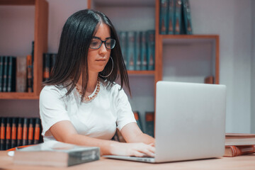 Chica joven con gafas estudiando para el examen en la biblioteca del campus universitario con...