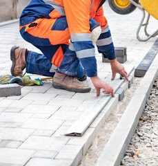 A worker measures a piece of paving slabs for leveling on the sidewalk. Vertical image.