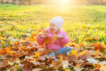 Happy young girl playing under falling yellow leaves in beautiful autumn park on nature walks outdoors. Little child throws up autumn orange maple leaves. Hello autumn concept.