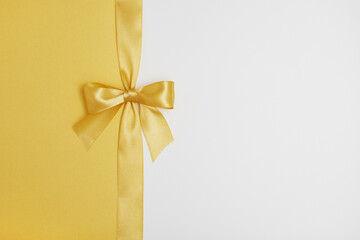 Shiny golden gift ribbon bow on white and yellow background