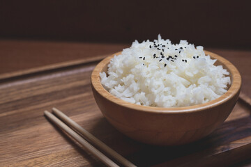 White rice (Jasmine rice) in wooden bowl and chopsticks with sesame seeds on wood board