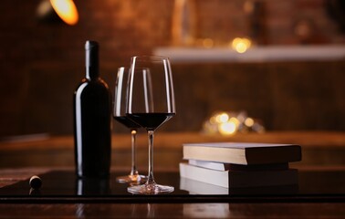 Glasses of red wine, some books with on table at home. Dark and warm colors, autumn mood.