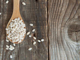 Obraz na płótnie Canvas raw pearl barley in a wooden spoon spilling on an old wooden table