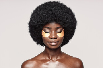 Portrait of beautiful young African woman with patches near eyes standing against gray background