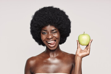 Portrait of beautiful young African woman holding green apple and winking