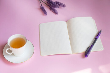 An empty open notebook. A cup of green, lavender flower. Pink background. Top view image of open notebook with blank pages, ready for adding text or mock up. Copy space. Selective focus