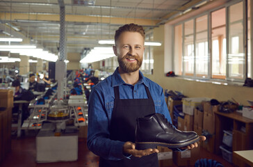 Proud happy male worker or director of a shoe factory shows off one shoe from a new collection of classic black leather men's shoes. Modern footwear manufacturing and business concept.