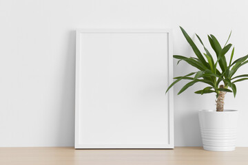 White frame mockup with a yucca plant on the wooden table.