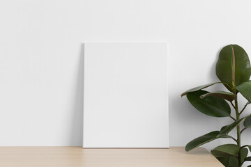 White canvas mockup on the wooden table with a ficus plant.
