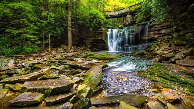 Low angle ground level view timelapse time lapse of Elakala waterfall in Blackwater Falls state park in West Virginia in autumn with colorful leaves foliage over bridge and swirling pool stream
