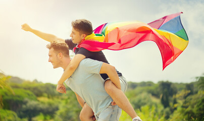 Happy young couple, gay family with flying LGBT rainbow flag having fun outdoors. Joyful gay men...