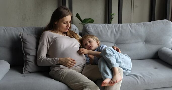 35s pregnant with second child woman spend time with little preschooler son talking about his brother or sister enjoy communication rest on cozy sofa at home. Family, pregnancy, motherhood concept
