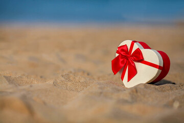 Gift box in the shape of a heart on the sea shore. Celebrating christmas, Valentine's day. Copy space.