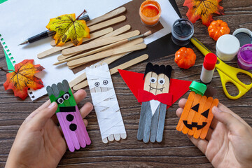 Child is holding Halloween ghost and vampire toy gift stics puppets on wooden table. Handmade....