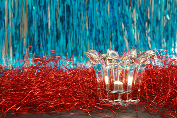 Lit candle in a transparent glass candlestick on a festive blue and red glitter background