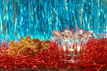 Lit candle in a transparent glass candlestick on a festive blue and red glitter background with...