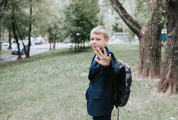 Fototapeta premium cute blond boy in a school uniform and with backpack on his shoulders goes to school at the beginning of the new school year, back to school concept and no desire to study