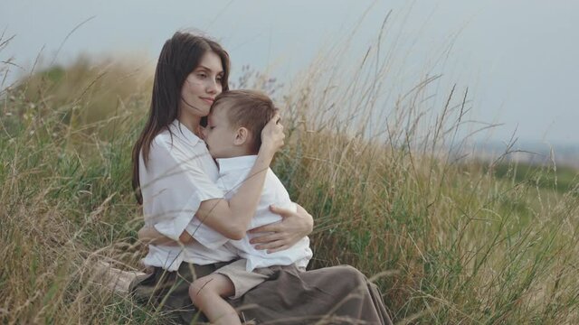 Happy mother hugging and kissing son while resting on hill