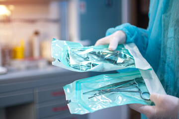 Close up of dentist hands in white sterile gloves holding dental tools for surgical use packed in a protective foil at dental office