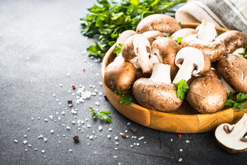 Raw mushrooms Champignon in wooden bowl with spices and herbs for cooking. Image with space for text.