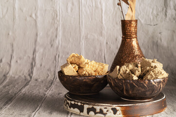 Oriental, traditional halva sweetness, two types of peanut and sunflower in ceramic bowls similar to coconut stand on a stand, behind a copper vase. Close-up, copy space..