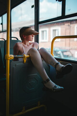 a girl with short hair, in a baseball cap, in a dress, is riding alone on a bus, a beautiful girl with short hair, wearing a hat on the bus smiles